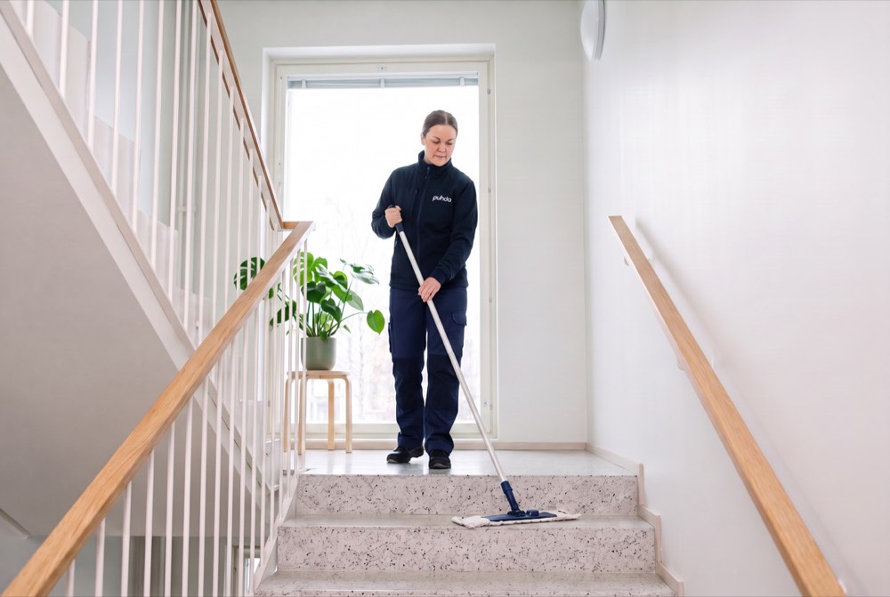 PUHDA-siivooja moppaa porraskäytävän terrazzo-portaita skandinaavisessa kerrostalossa